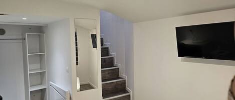 A modern bedroom with a built-in wardrobe, a staircase, and a mounted TV.