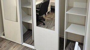 Una habitación con cama, escritorio y silla, con puerta de armario corredera y un armario blanco.