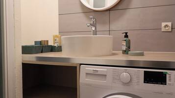 Ein kleines Badezimmer mit Waschmaschine, Waschbecken und Spiegel.