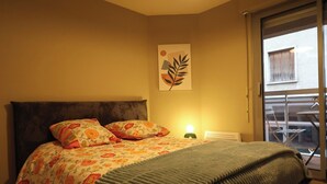 Ein Schlafzimmer mit einem Bett, floralem Bettzeug, einem Nachttisch mit Lampe und einem Fenster mit Blick nach draußen.