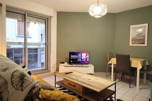 Ein Wohnzimmer mit Fernseher, einem Esstisch und einer Couch.