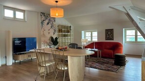 Ein modernes Wohnzimmer mit Essbereich, einem roten Sofa, einem Fernseher und einem großen Fenster.