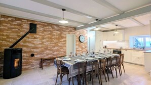 Ein Essbereich mit Backsteinwand, einem großen Esstisch, der für eine Mahlzeit gedeckt ist, und einer Küche im Hintergrund.