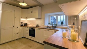 Eine moderne Küche mit weißen Schränken, einer Holzarbeitsplatte und einem eingebauten Backofen. Auf der Arbeitsplatte stehen drei Glasbehälter mit Kerzen.