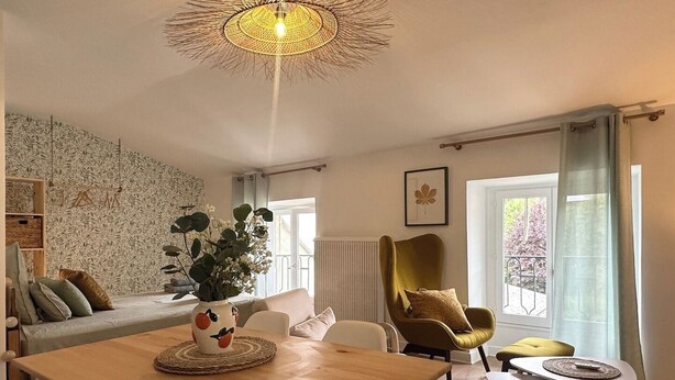 Un salon chaleureux avec une table à manger en bois, un canapé, un fauteuil vert et une grande fenêtre avec des rideaux.