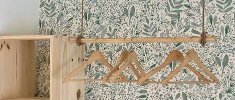 A wooden hanger rack with three hangers against a wall with a leafy pattern wallpaper.