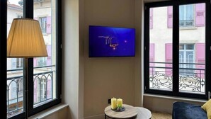 A room with a TV mounted on the wall, a small round table with candles, and large windows with balconies.