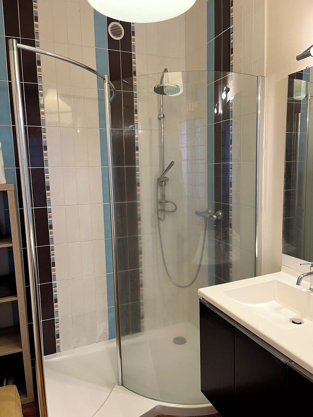A modern bathroom with a glass-enclosed shower, a white sink, and a large mirror.
