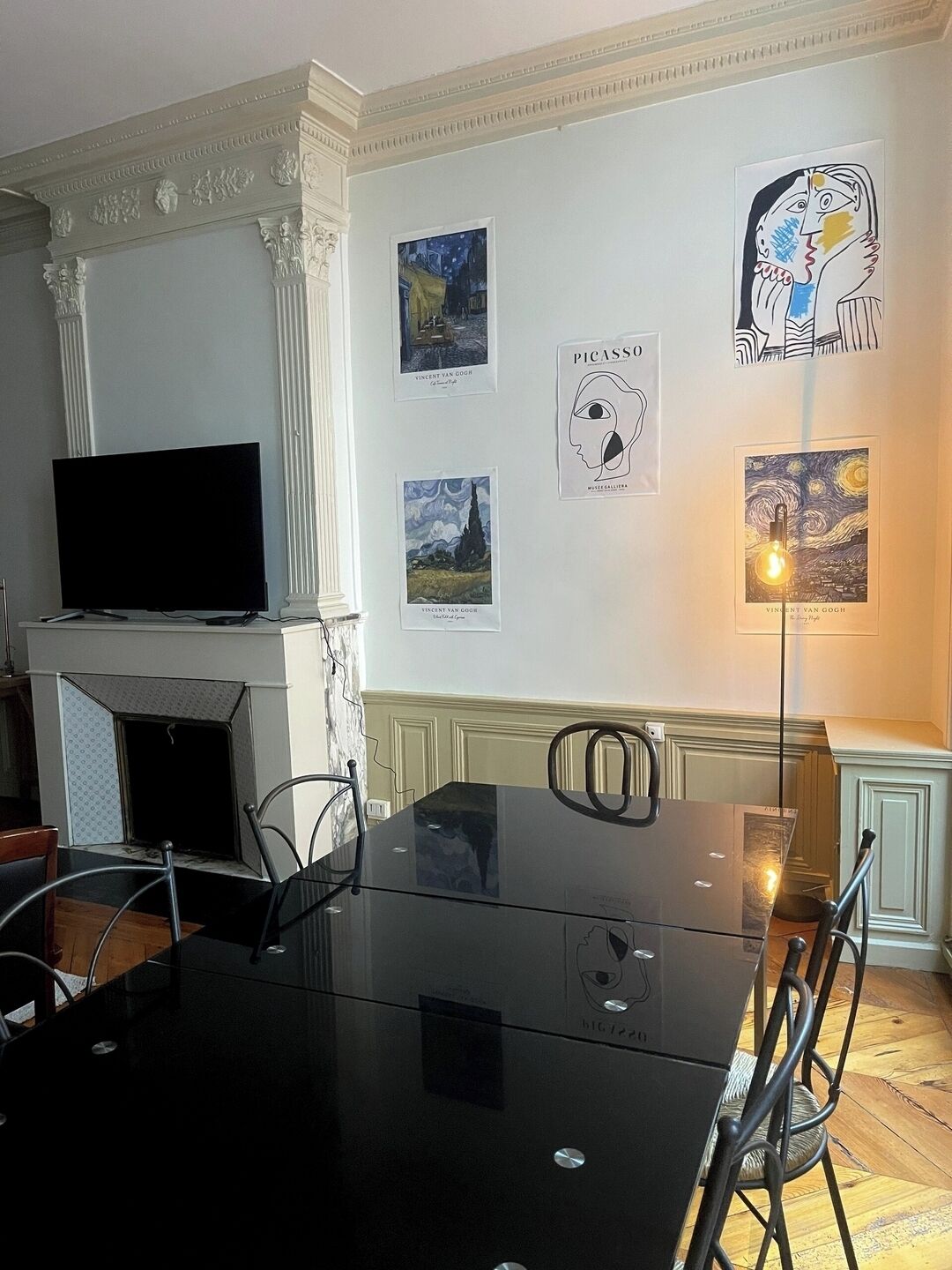 Un coin repas avec une table en verre noir, des chaises, un téléviseur à écran plat et des œuvres d’art accrochées aux murs.