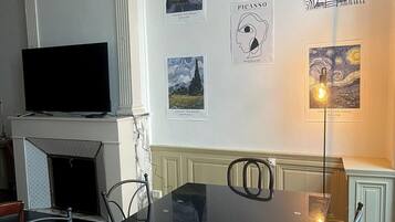 Un coin repas avec une table en verre noir, des chaises, un téléviseur à écran plat et des œuvres d’art accrochées aux murs.