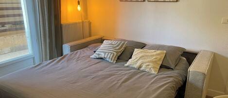 Una cama bien hecha con una colcha gris y dos almohadas, una mesita de noche con una lámpara y dos cuadros abstractos colgados en la pared.