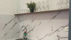 Eine Küche mit Marmorfliesen an der Rückwand, einem Spülbecken und einem Regal mit Gläsern und einer Pflanze.