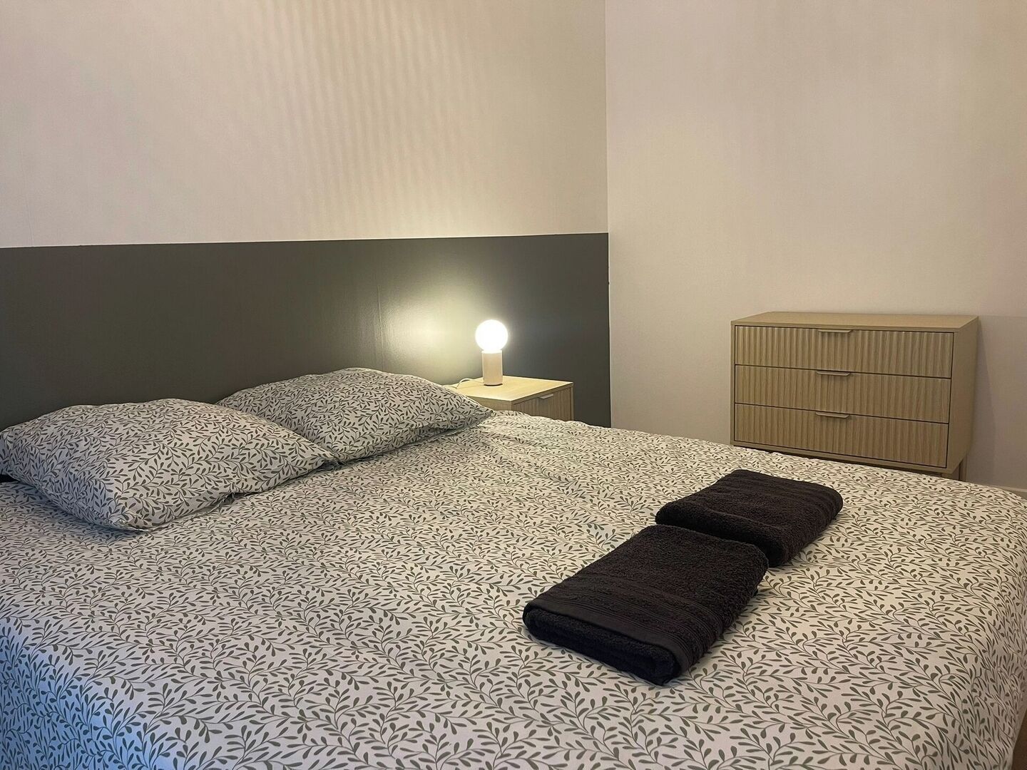 Un lit bien fait, avec une literie à motifs, une lampe de chevet et une table de chevet en bois.