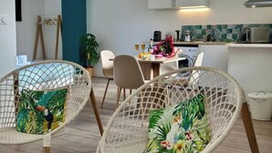 Une cuisine moderne avec des meubles blancs, une table à manger avec des chaises et une plante suspendue.