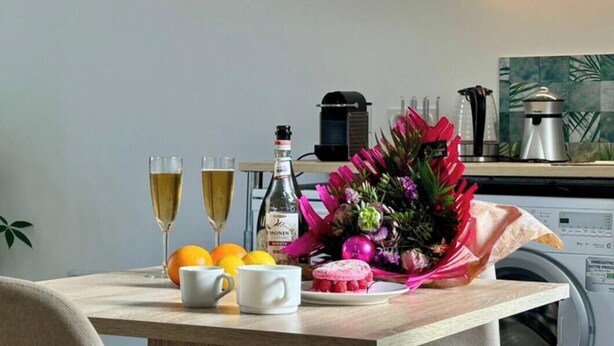 Une table à manger avec deux coupes de champagne, une bouteille de Monin, un bouquet de fleurs et une assiette contenant une pâtisserie.