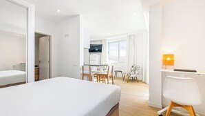 A modern hotel room with a large bed, a desk with a chair, a dining table with chairs, and a kitchen area in the background. - Step To The Sea 5, by Pausa Holiday Rentals (Funchal)