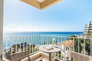 Uma varanda com mesa, cadeiras e vista para o mar.