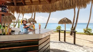 A bar area with a view of the beach and ocean, featuring a thatched roof and wooden beams. - Dreams La Romana All Inclusive Resort & Spa (San Rafael del Yuma)