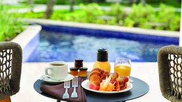 Desayuno con croissant, fruta y zumo de naranja sobre una mesa junto a una piscina.