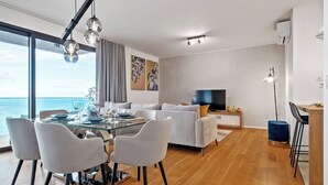 A modern living room with a glass dining table, grey sofas, and a flat-screen TV. - Ajuda I - Penthouse by Pausa Holiday Rentals (Funchal)