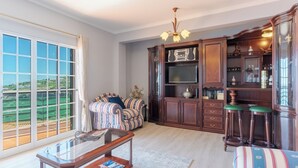 Un salón amplio con un gran ventanal, un sofá, una mesa de centro y un aparador de madera con un televisor.