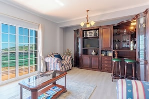 A spacious living room with a large window, a sofa, a coffee table, and a wooden cabinet with a television. - Alegria Apartment, by Pausa Holiday Rentals (Estreito da Calheta)