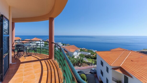 Un balcón con vistas al mar, suelo de baldosas y una mesa con sillas.