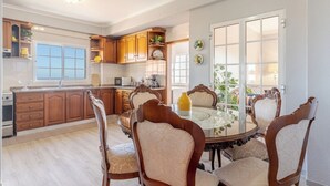 Un comedor con una mesa redonda y seis sillas, una cocina con armarios de madera y vistas a través de un ventanal.