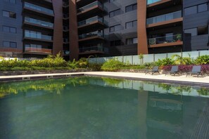 A modern building with a swimming pool, surrounded by lush greenery and lounge chairs. - Renala II - Apart, With Pool, by Pausa H. Rentals (Funchal)
