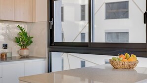 Una cuina amb una finestra gran, una planta en test i una cistella de fruita sobre el taulell.