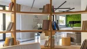 Un interior modern amb una biblioteca de fusta plena de llibres, un rètol que diu "S. LUCAS RESIDENCE" i una paret verda amb un piano.