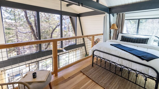 Een slaapkamer met een groot raam, een bed, een tafeltje en een stoel.
