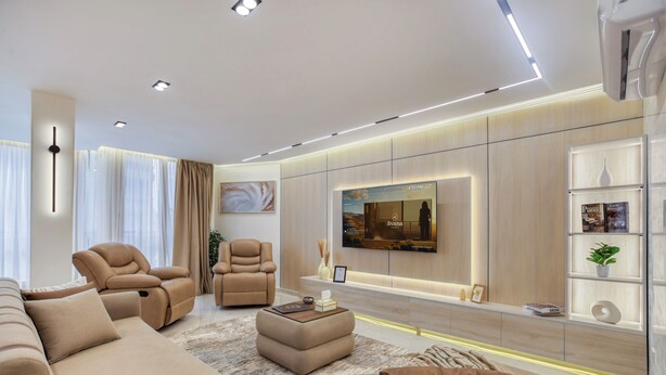 Ein modernes Wohnzimmer mit einer Couch, zwei Relaxsesseln, einem Couchtisch und einem an der Wand montierten Fernseher.
