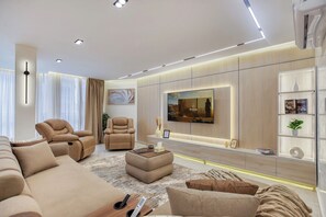 Una sala moderna con un sofá, dos sillones reclinables, una mesa de centro y un televisor montado en la pared.