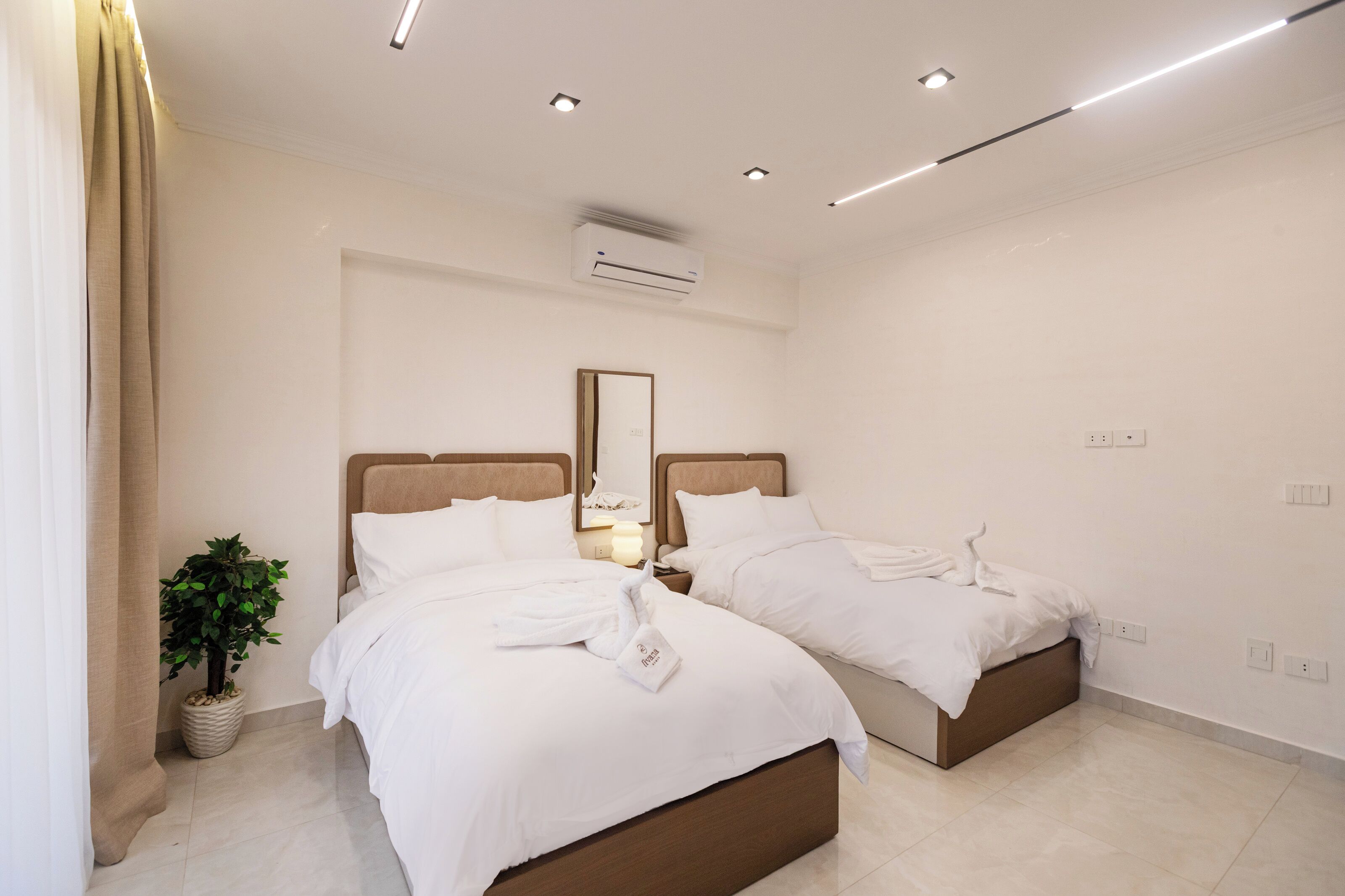 Une chambre d’hôtel moderne avec deux lits, une plante en pot, un appareil de climatisation et un miroir au mur.