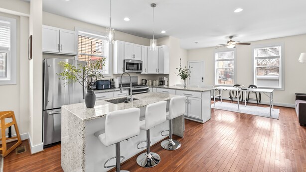 Una cocina moderna con electrodomésticos de acero inoxidable, armarios blancos y una isla central con taburetes de bar.