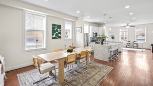 Una cocina moderna con armarios blancos, una isla central y un comedor con una mesa y sillas de madera.