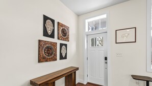 Un pasillo con una consola de madera, una puerta blanca y cuatro obras de arte colgadas en la pared.