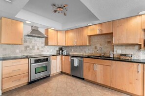 A modern kitchen with wooden cabinets, a stainless steel oven, and a dishwasher. - Spacious Beachfront Condo with Stunning Gulf Views (Indian Rocks Beach)