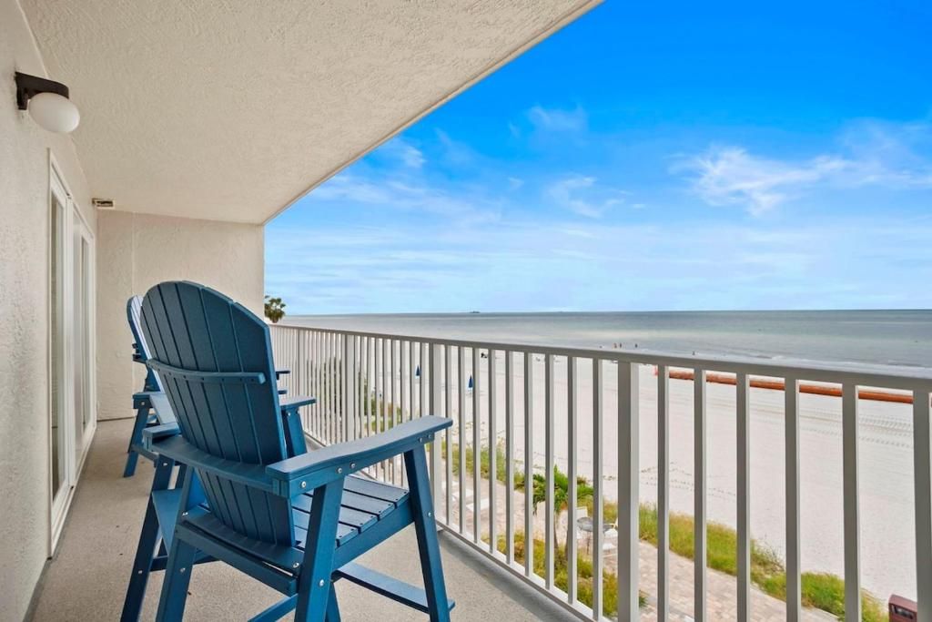 Un balcón con vista a la playa y una silla Adirondack azul.