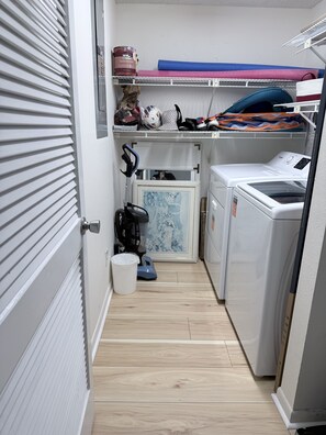 A laundry room with a washing machine, dryer, and a vacuum cleaner. - Direct Gulf-Front 3BR, Sleeps 8  Huge Balcony, Pool & Private Garage (Indian Rocks Beach)