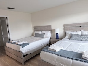 A hotel room with two beds, wooden headboards, a nightstand with a lamp, and a door with louvered shutters. - Direct Gulf-Front 3BR, Sleeps 8  Huge Balcony, Pool & Private Garage (Indian Rocks Beach)