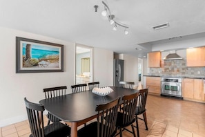 A modern kitchen with stainless steel appliances, a dining area with a dark wooden table and chairs, and a framed painting on the wall. - Spacious Beachfront Condo with Stunning Gulf Views (Indian Rocks Beach)