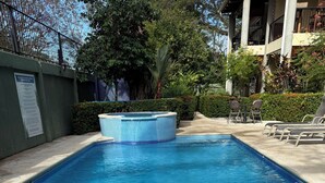 Ein Schwimmbecken mit Whirlpool, umgeben von Liegestühlen und einer Betonplattform.