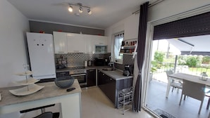 A modern kitchen with a dining area, a refrigerator, a coffee maker, and a view of the outdoors. - Villa Madlen - Deluxe Poolside Apartment (Opatija)