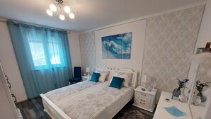 A bedroom with a large bed, two bedside tables, a chair, a mirror, and a decorative rug. - Villa Madlen - Deluxe Poolside Apartment (Opatija)