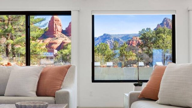 Una sala de estar moderna con suelo de piedra, dos sofás, una mesa de centro y grandes ventanales con vista a la montaña.