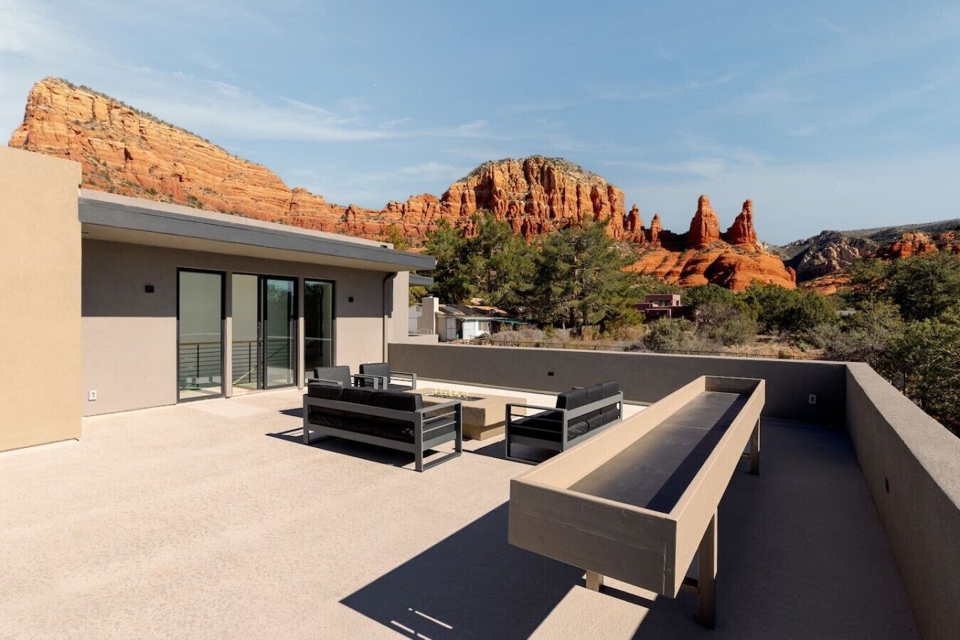 A modern outdoor patio with a minimalist design, featuring a seating area and a glass door leading to a covered entrance.