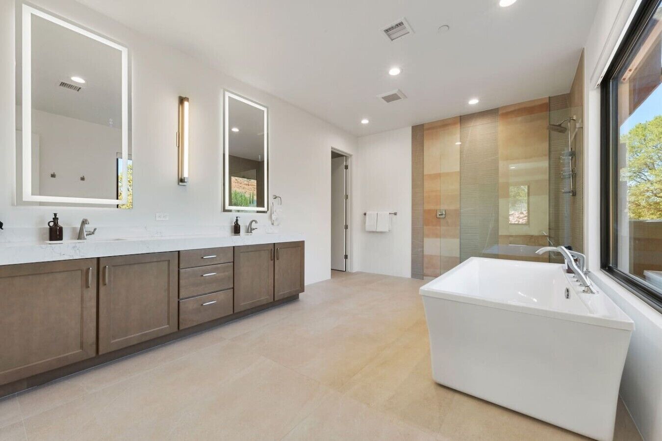 Un bagno moderno con una vasca da bagno ampia, un doppio lavabo con specchi e un box doccia in vetro.