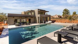 Una casa moderna de dos pisos con piscina, mobiliario exterior y vistas del paisaje circundante.